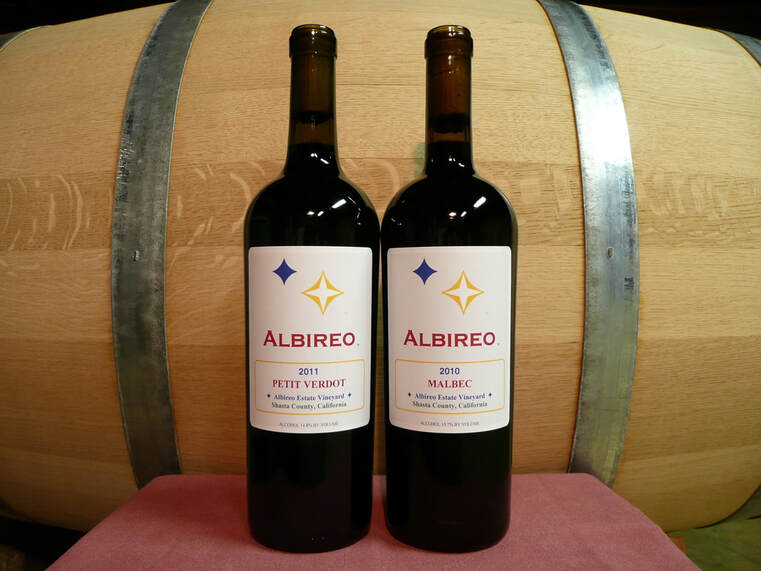Photo of two Albireo wine bottles in front of a barrel.